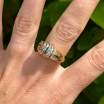 Hand wearing a gold ring with diamonds against a blurred green leafy background