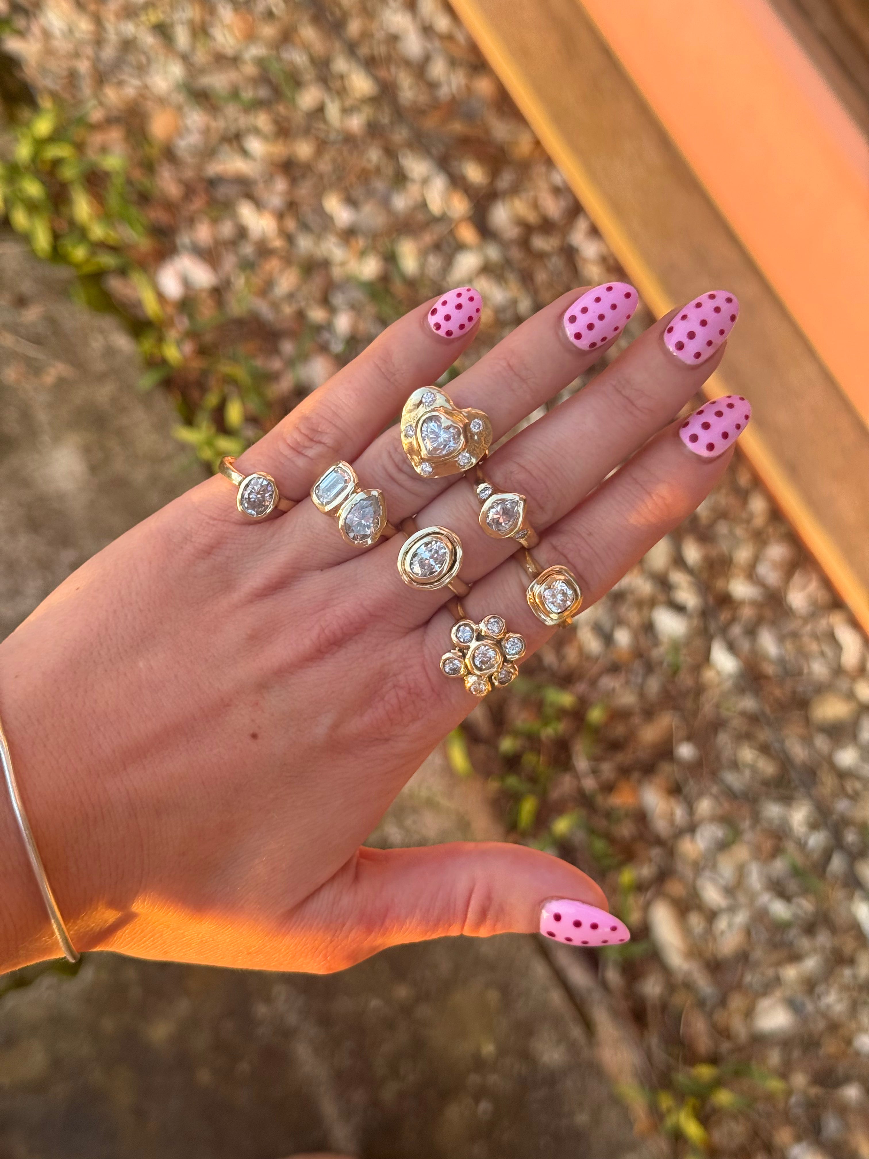 Hand wearing multiple rings with pink polka dot nail polish on a natural background