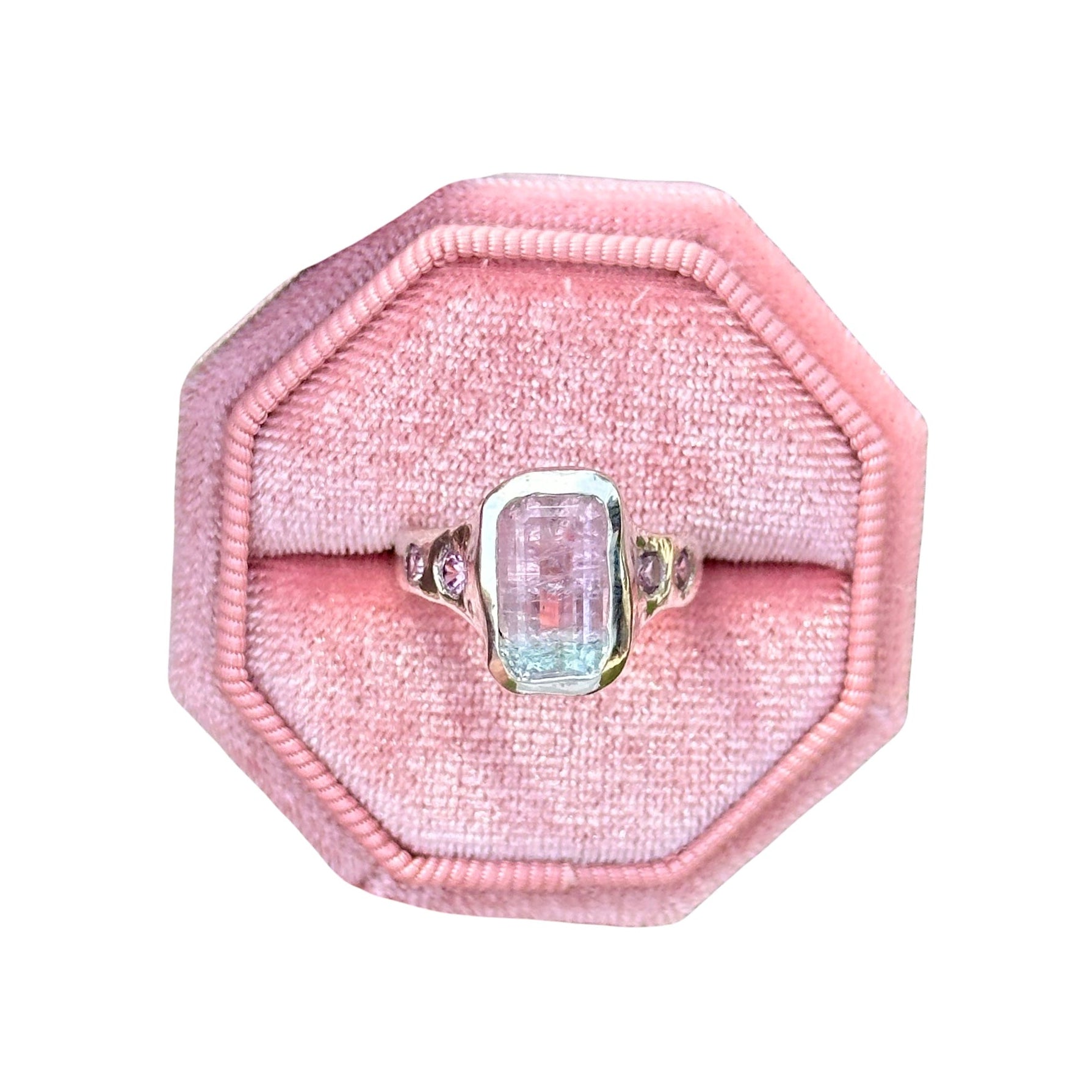 Ring with a pink gemstone in a pink velvet box on a white background