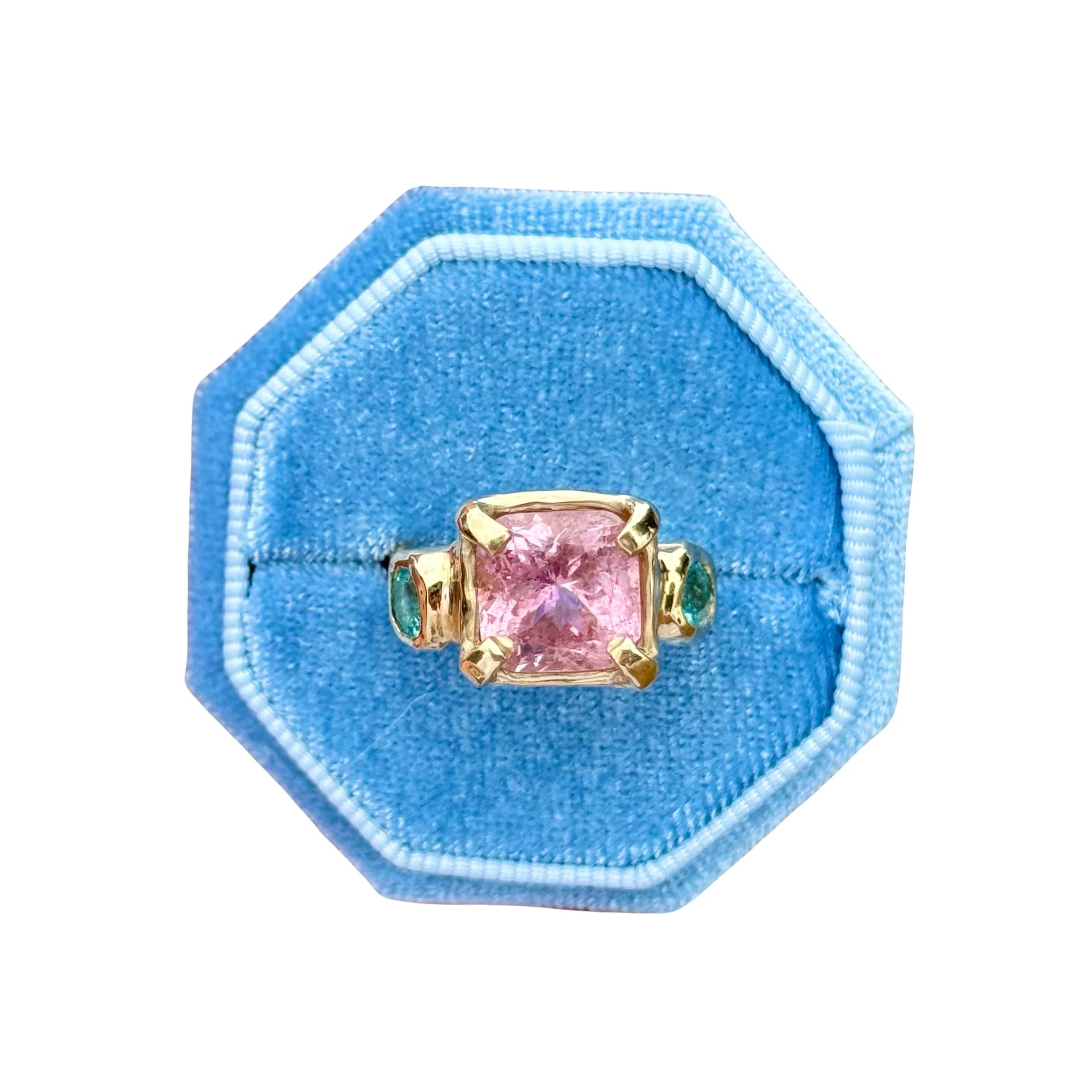 Ring with pink gemstone in a blue velvet box on a white background