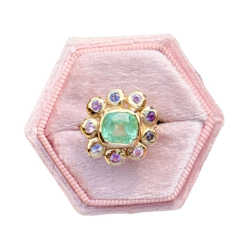 Hexagonal pink velvet jewelry box with a green gemstone ring on a white background