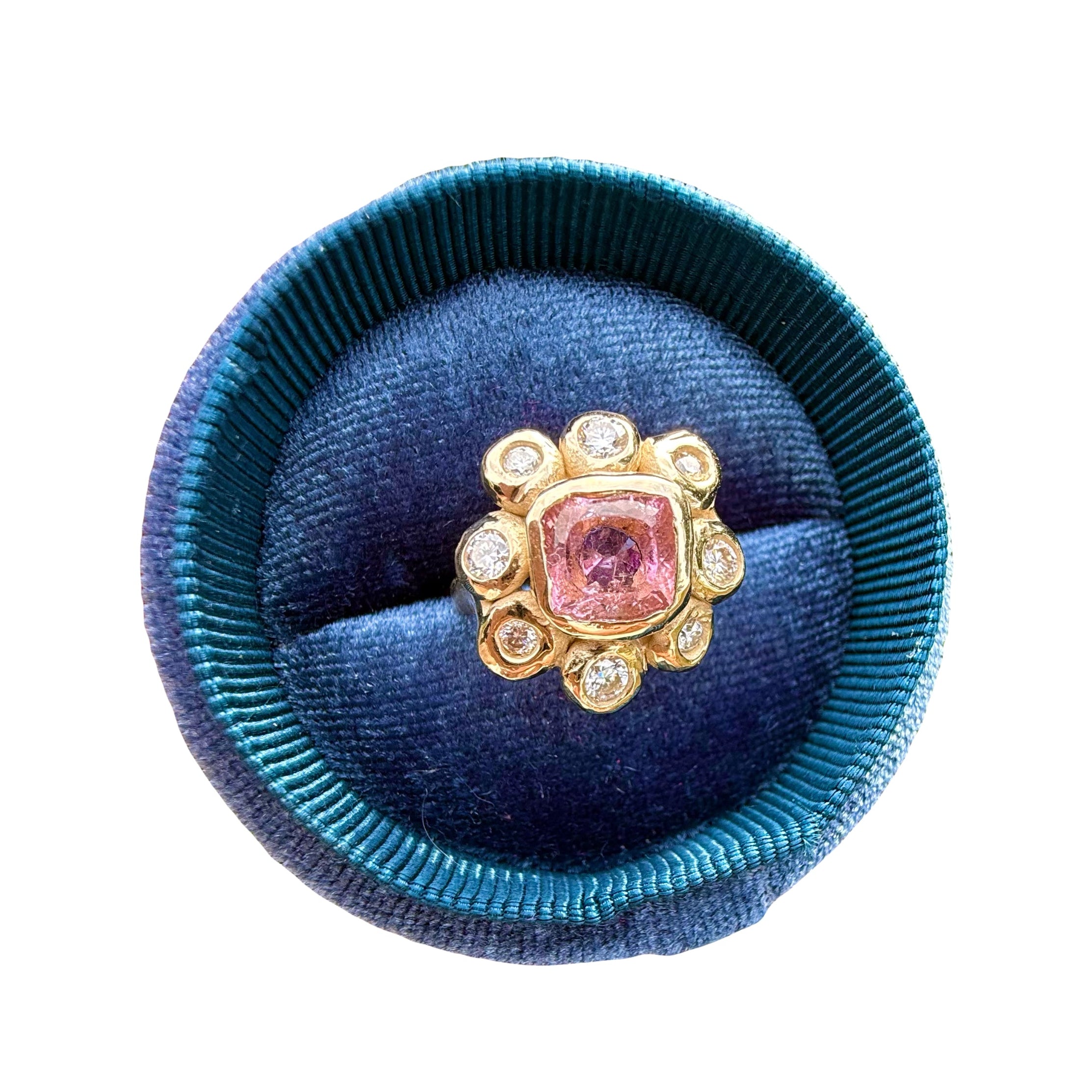 Ring with a pink gemstone in a blue velvet cushion on a white background