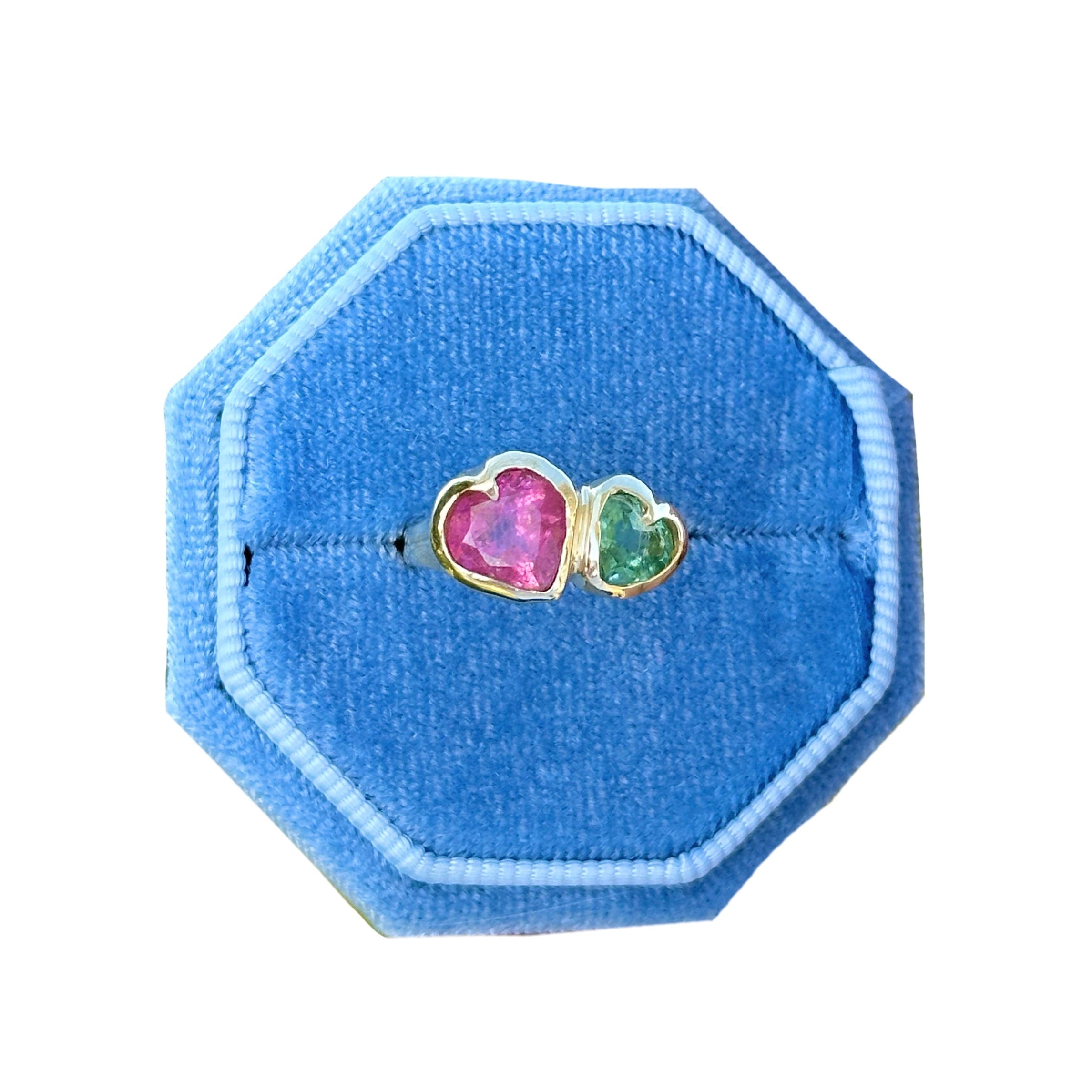 Two heart-shaped rings on a blue octagonal ring holder against a white background