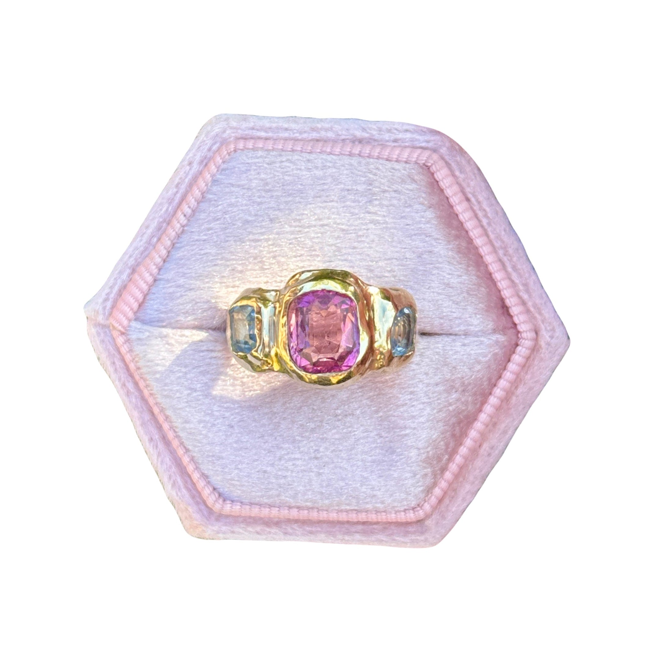 Gold ring with a pink gemstone in a hexagonal pink velvet box on a white background