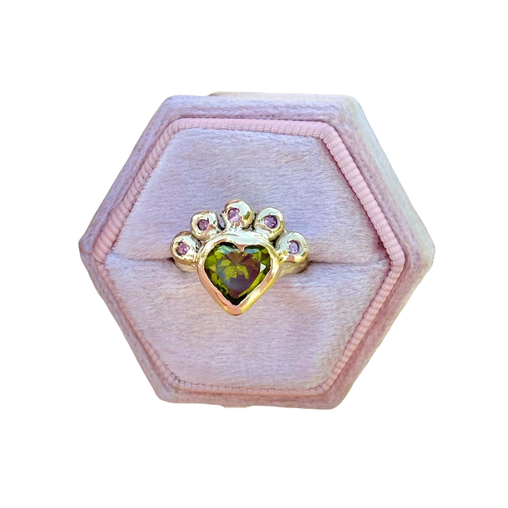 Hexagonal pink jewelry box with a ring featuring a green gemstone on a white background