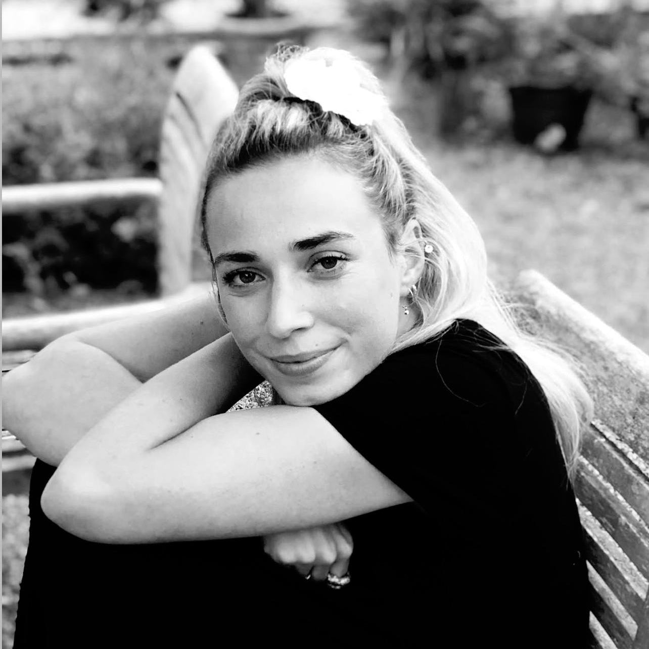 Black and white photo of a woman sitting outdoors with a blurred background